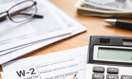 Temporada de impuestos 2026: Formulario W-2 parcialmente visible junto a una calculadora y lápiz sobre un escritorio.