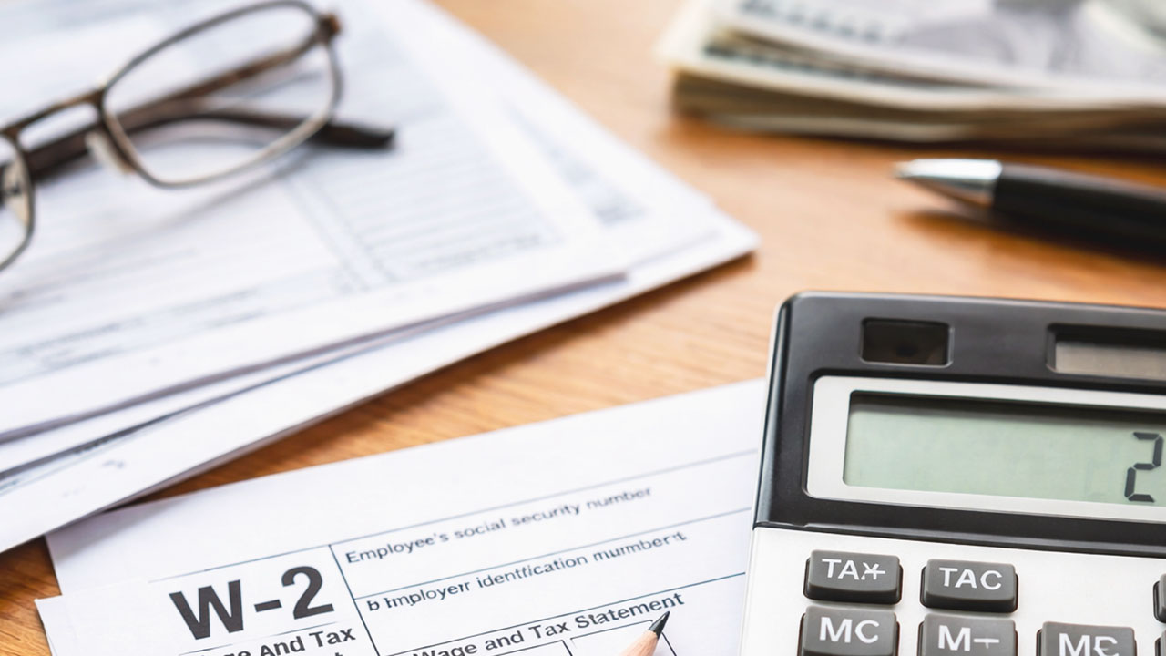 Temporada de impuestos 2026: Formulario W-2 parcialmente visible junto a una calculadora y lápiz sobre un escritorio.