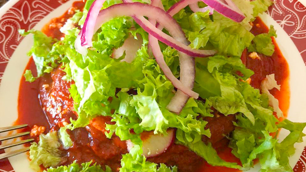 Enchiladas sonorenses servidas en un plato, acompañadas de verdura, queso y crema.